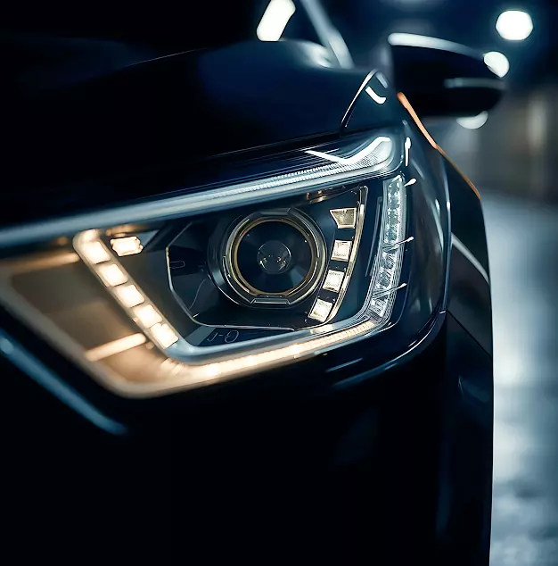Primo piano di un faro di automobile moderno, con luci a LED e design elegante, evidenziando dettagli costruttivi e riflessi.